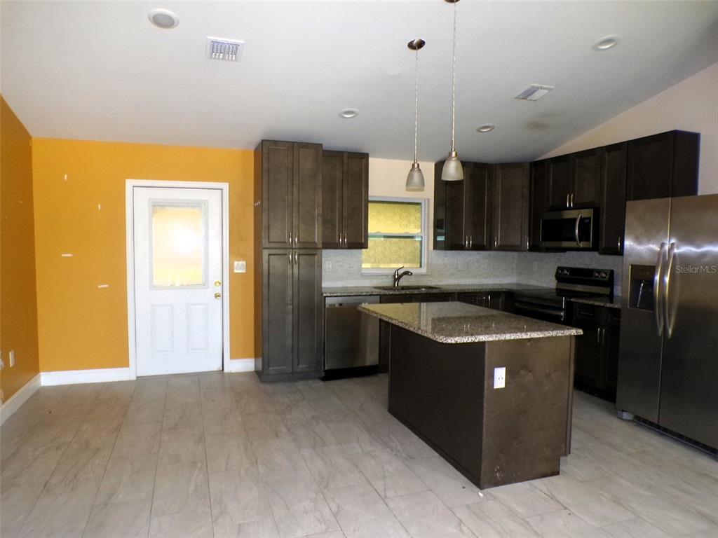 A kitchen features dark wood cabinets, granite countertops, a center island, and a yellow wall — 3724 TRACY STREET, FORT MYERS, FL