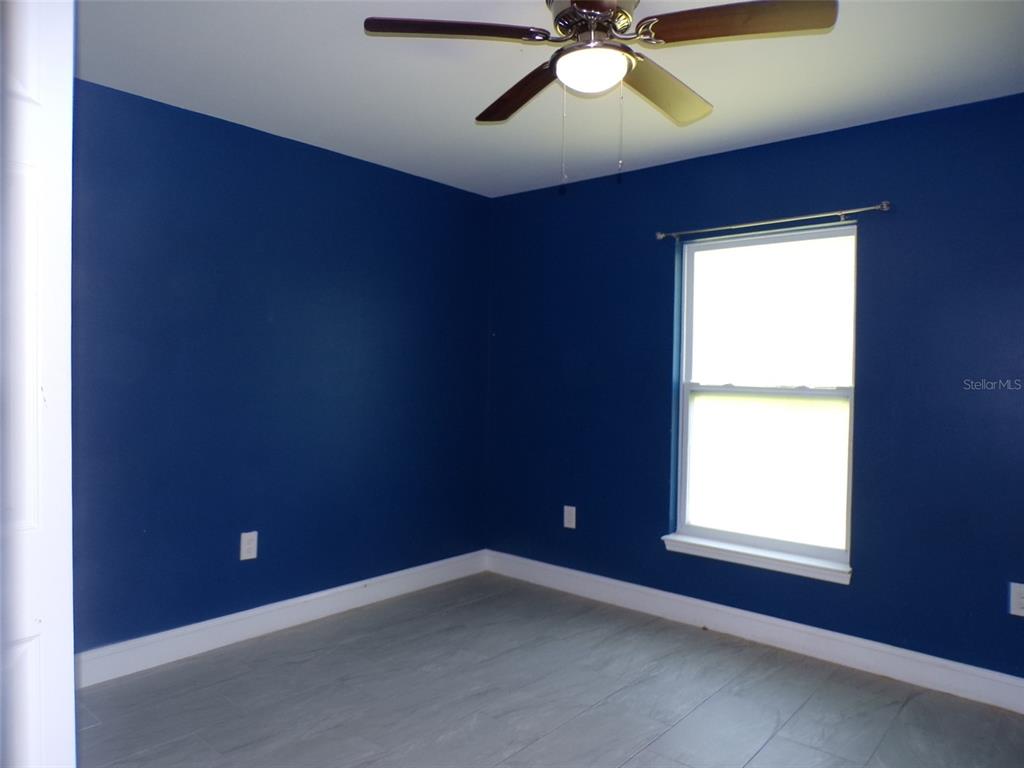 A bedroom with dark blue walls, light gray wood-look flooring, and a ceiling fan — 3724 TRACY STREET, FORT MYERS, FL