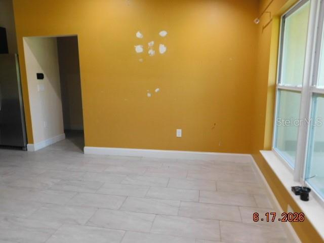 A room with yellow walls, light-colored tile flooring, and a doorway leading to a kitchen — 3724 TRACY STREET, FORT MYERS, FL