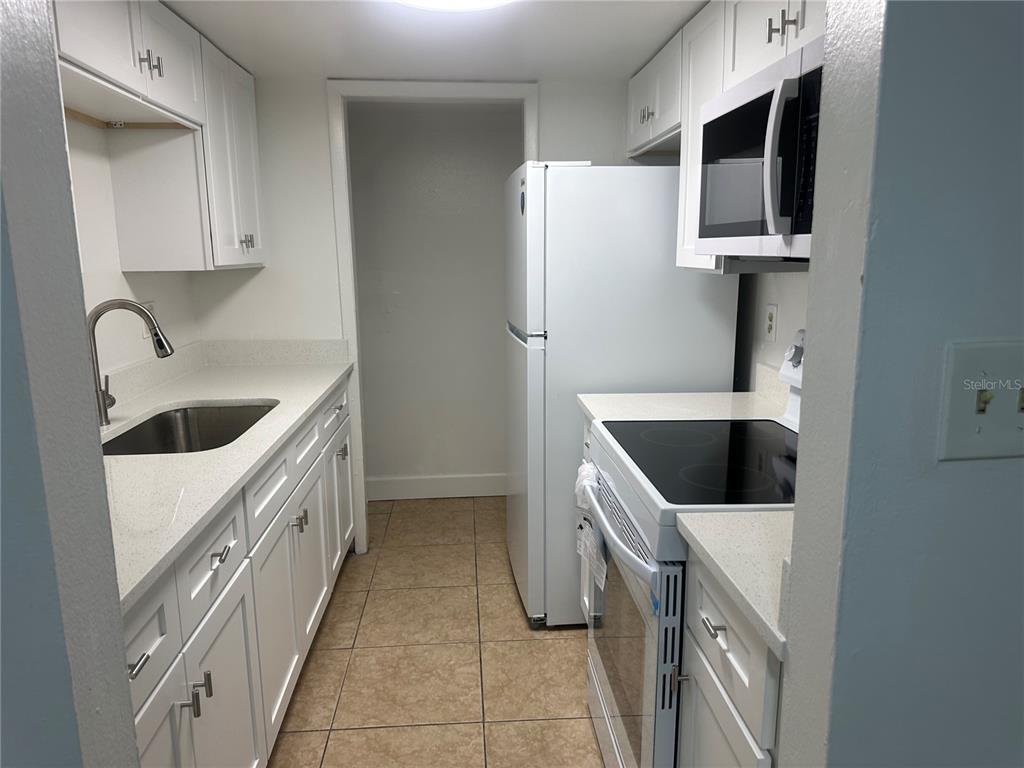 A galley kitchen features white cabinets, light countertops, stainless steel appliances, and tiled flooring — 8426 CAMDEN STREET UNIT A, TAMPA, FL