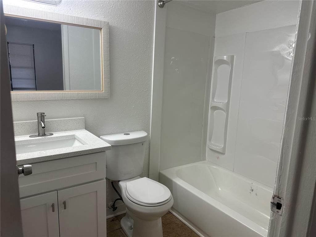 A bathroom features a white vanity, a toilet, and a shower-tub combination with white walls — 8426 CAMDEN STREET UNIT A, TAMPA, FL