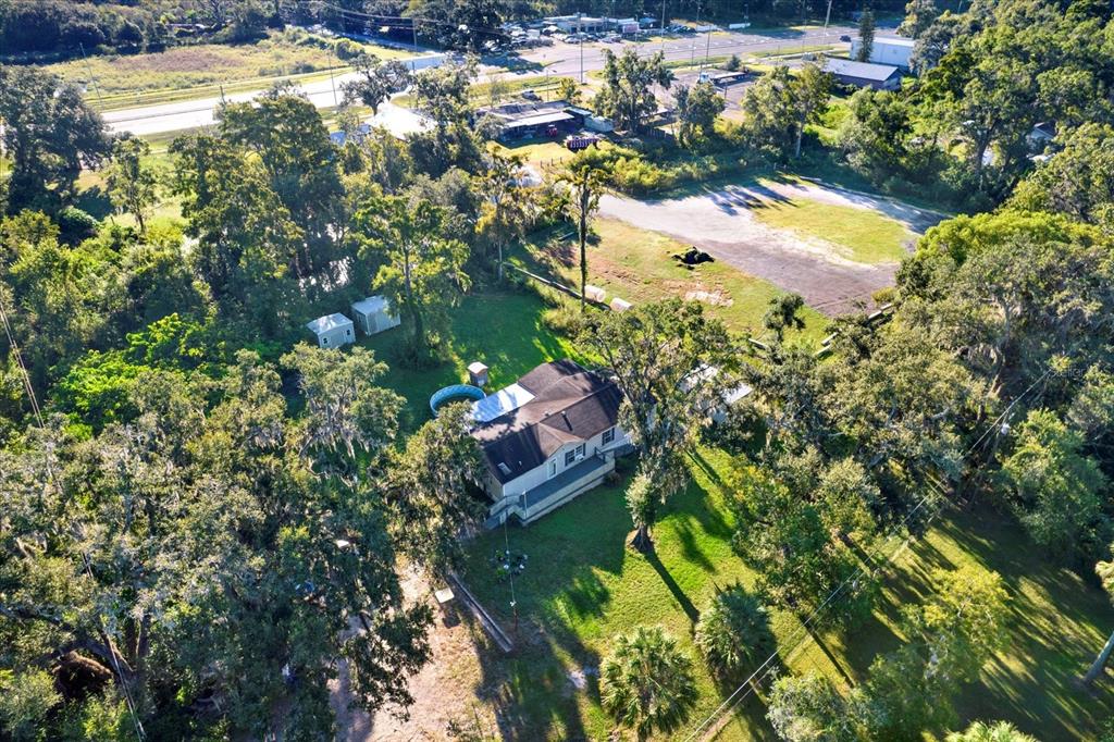 An aerial view shows a house with a pool and sheds on a wooded lot — 9211 HARNEY BAPTIST CHURCH ROAD, TAMPA, FL