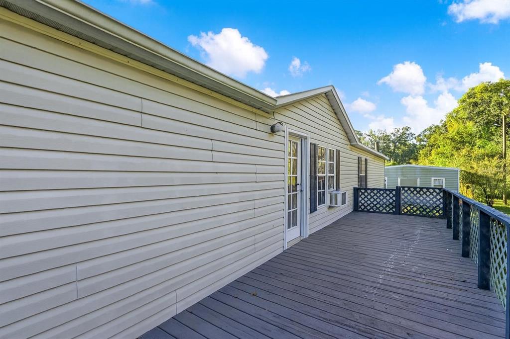 A wide wooden deck runs along the side of a beige vinyl-sided mobile home — 9211 HARNEY BAPTIST CHURCH ROAD, TAMPA, FL