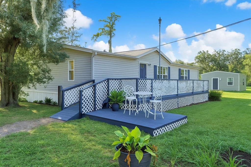 A light gray manufactured home features a blue deck with lattice railings and outdoor furniture — 9211 HARNEY BAPTIST CHURCH ROAD, TAMPA, FL