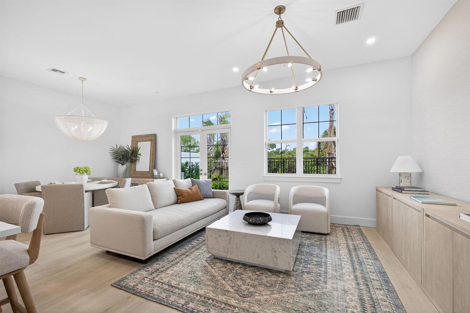 A bright living and dining area features a marble coffee table, neutral furniture, and chandeliers — 115 Water Pointe Place # 34, Jupiter FL 33477, JUPITER, FL