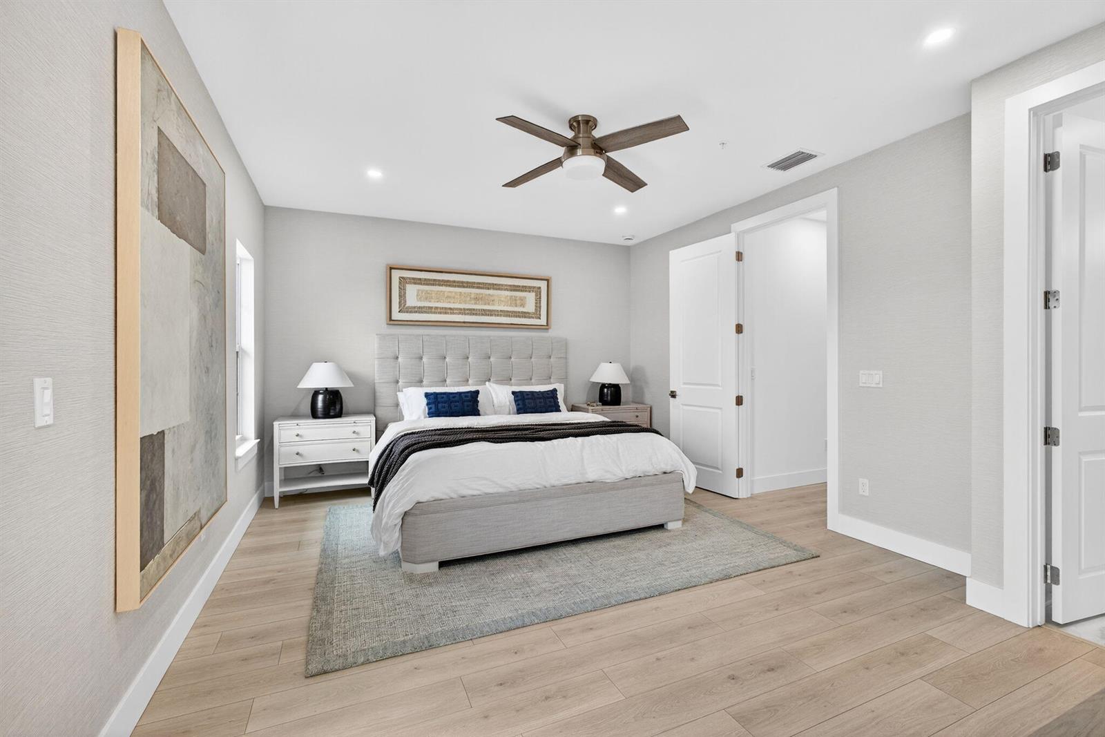 A bedroom features a tufted headboard, light wood flooring, a ceiling fan, and neutral walls — 115 Water Pointe Place # 34, Jupiter FL 33477, JUPITER, FL