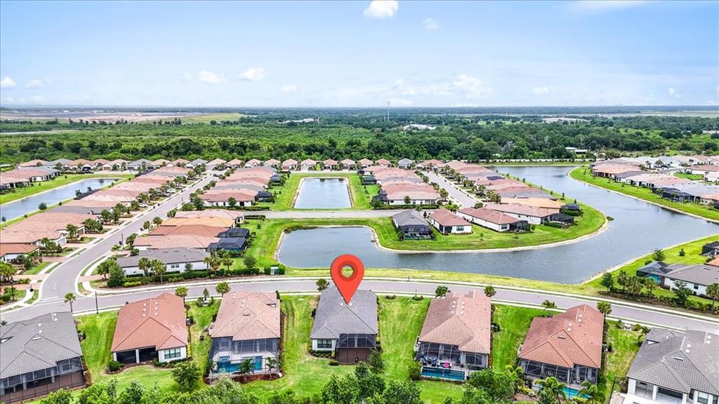 An aerial view shows a suburban neighborhood with houses surrounding a central pond — 11014 WICKER PARK PLACE, PALMETTO, FL
