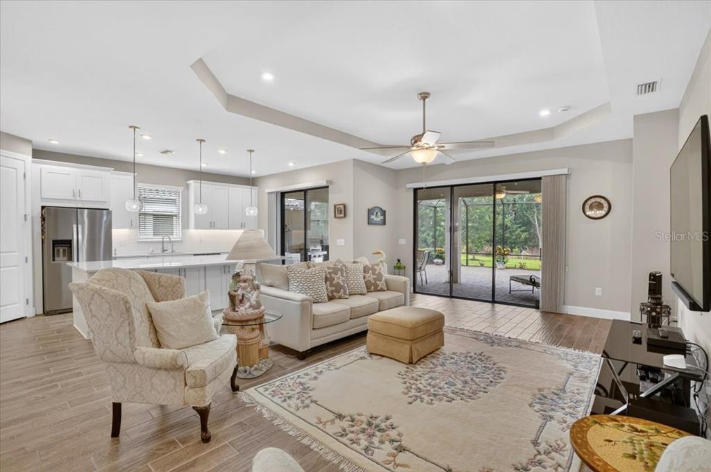 An open-concept living room features a tray ceiling, tile flooring, and sliding glass patio doors — 11014 WICKER PARK PLACE, PALMETTO, FL