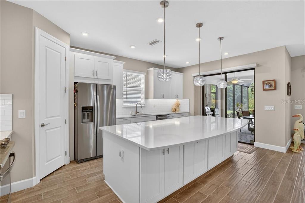 A modern kitchen features a large white island, stainless steel appliances, and wood-look tile flooring — 11014 WICKER PARK PLACE, PALMETTO, FL