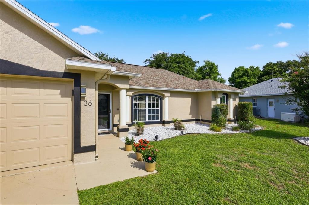 A tan single-story house exterior features a garage, front entryway, and a landscaped yard — 36 FORGE LANE, PALM COAST, FL