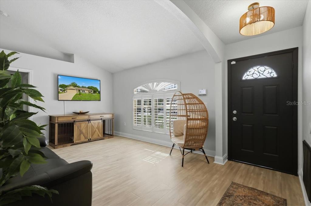 A living room features light wood-look flooring, a black front door, and a wicker chair — 36 FORGE LANE, PALM COAST, FL
