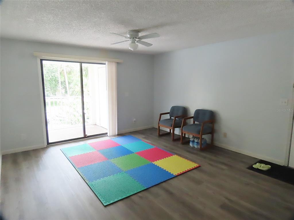 A living room features light gray walls, wood-look flooring, a ceiling fan, and sliding glass doors — 3108 OAK TRAIL RUN UNIT 3108, PORT ORANGE, FL