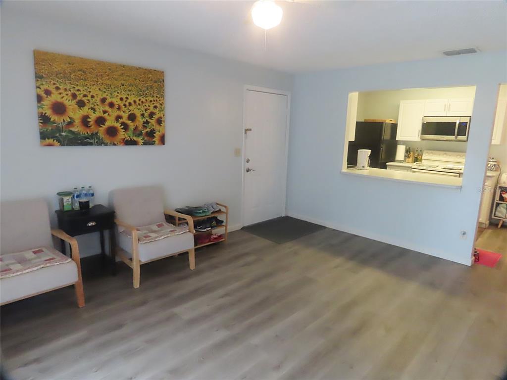 A living room with light wood-look flooring, two armchairs, a sunflower painting, and a kitchen pass-through — 3108 OAK TRAIL RUN UNIT 3108, PORT ORANGE, FL