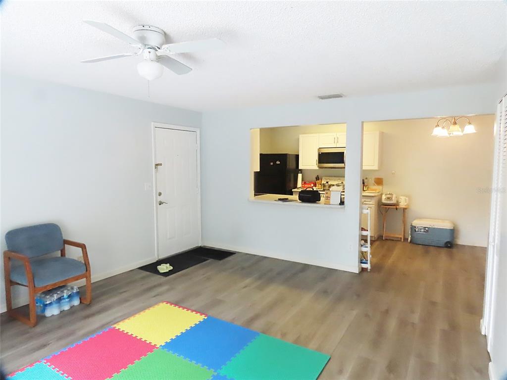 A living room with light gray walls, wood-look flooring, a ceiling fan, and a kitchen pass-through — 3108 OAK TRAIL RUN UNIT 3108, PORT ORANGE, FL