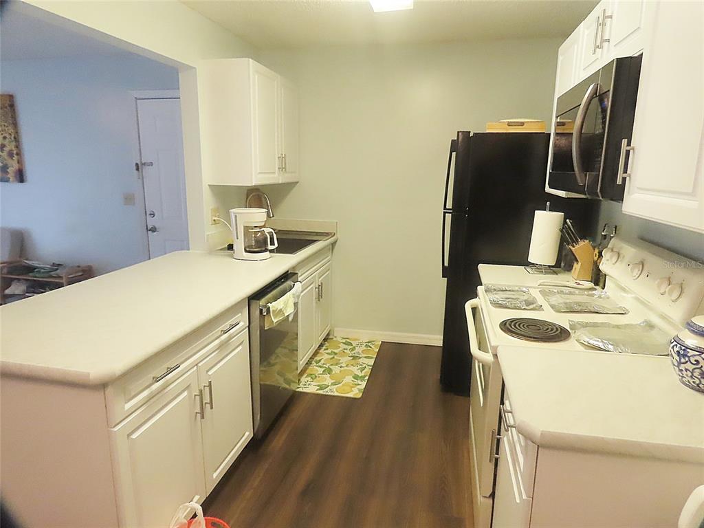 A kitchen features white cabinets, dark wood-look flooring, a black refrigerator, and a white stove — 3108 OAK TRAIL RUN UNIT 3108, PORT ORANGE, FL