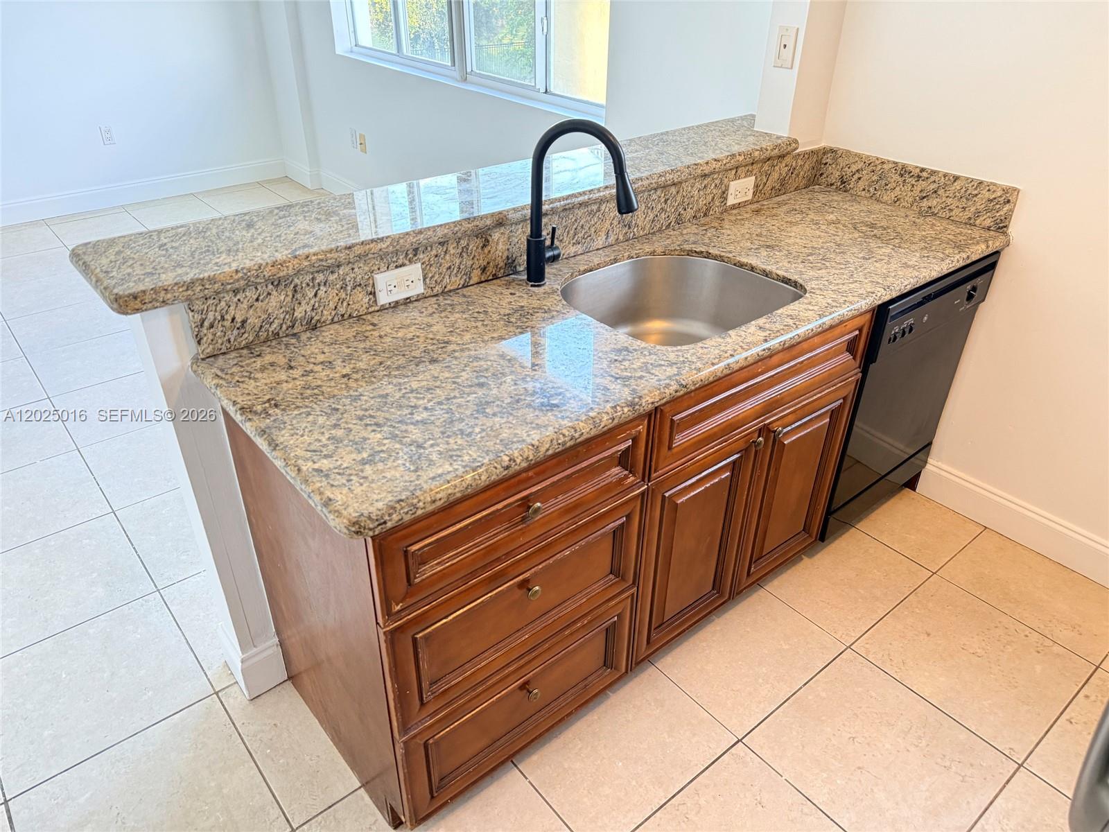 A kitchen sink with a black faucet is set into a granite countertop with wooden cabinets — 400 SW 2nd St # 201, Miami FL 33130, MIAMI, FL