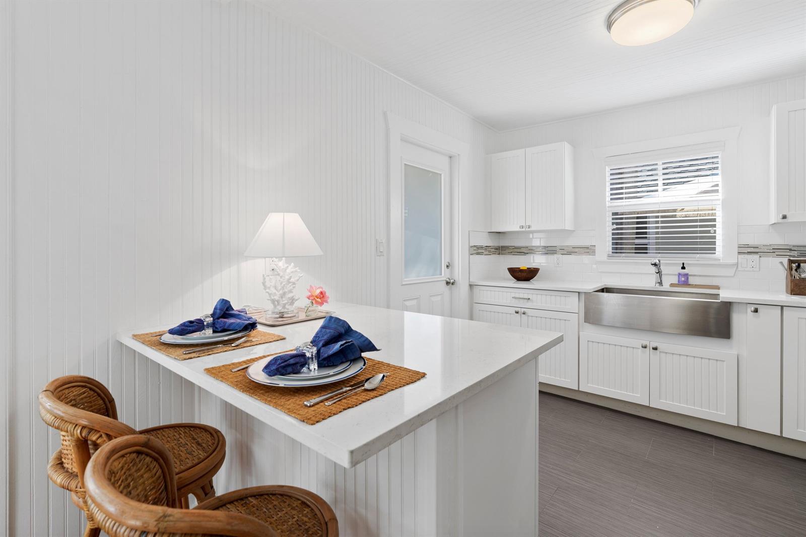 A white kitchen features a breakfast bar with two wicker chairs and a farmhouse sink — 118 SE 7th Avenue, Delray Beach FL 33483, DELRAY BEACH, FL