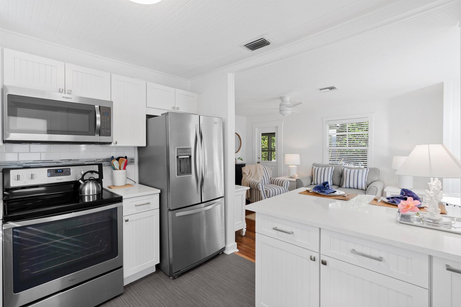 A kitchen with white cabinets, stainless steel appliances, and an island opens into a living area — 118 SE 7th Avenue, Delray Beach FL 33483, DELRAY BEACH, FL