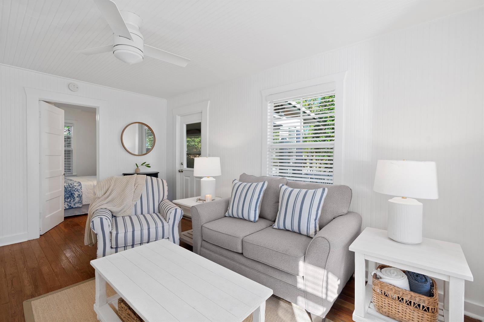 A living room with white beadboard walls, a gray sofa, striped armchair, and wooden floors — 118 SE 7th Avenue, Delray Beach FL 33483, DELRAY BEACH, FL