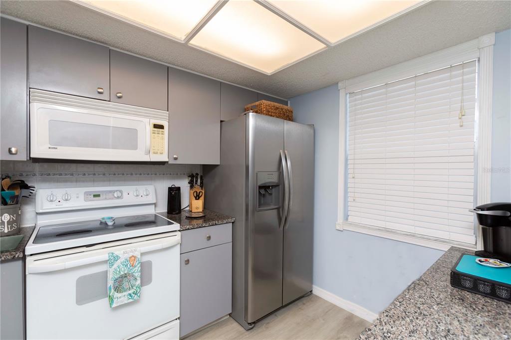 A kitchen features gray cabinets, stainless steel appliances, a white stove, and granite countertops — 11140 CARRIAGE HILL DRIVE UNIT 4, PORT RICHEY, FL