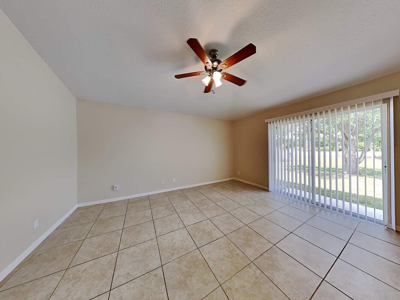 An empty room with beige tile flooring, a ceiling fan, and sliding glass patio doors — PORT ST. LUCIE, FL