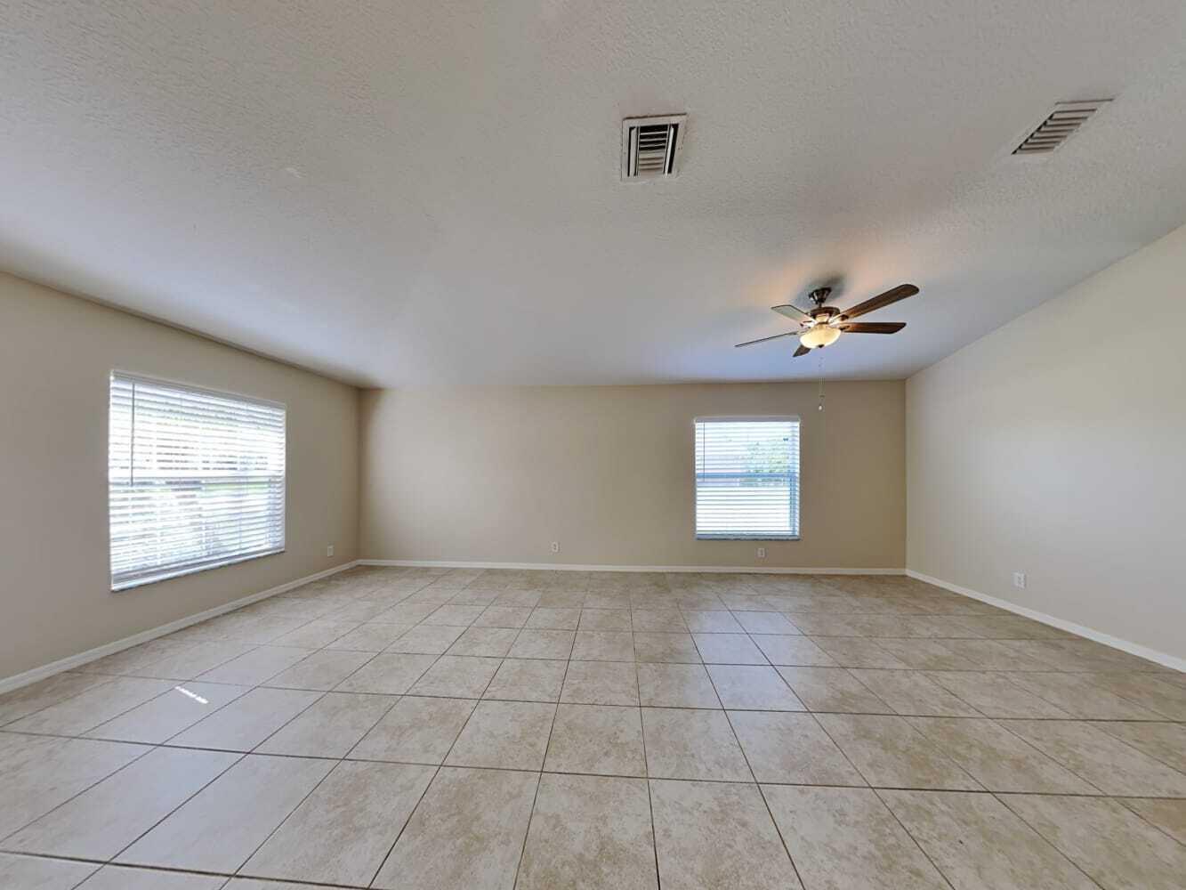 An empty room with beige tile flooring, two windows with blinds, and a ceiling fan — PORT ST. LUCIE, FL
