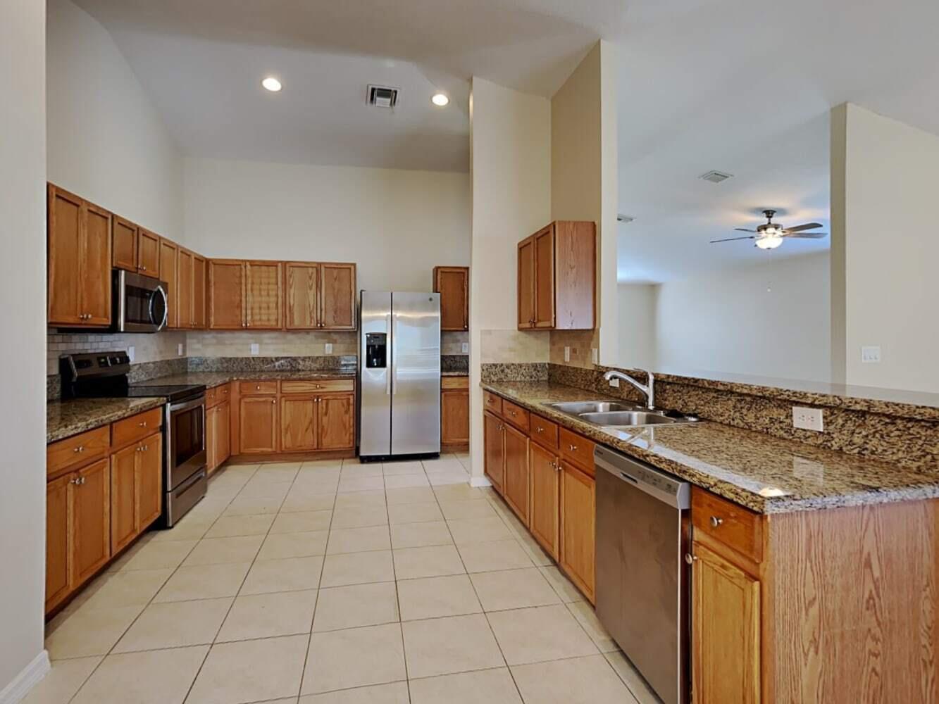 A kitchen with wood cabinets, granite countertops, stainless steel appliances, and light tile flooring — PORT ST. LUCIE, FL
