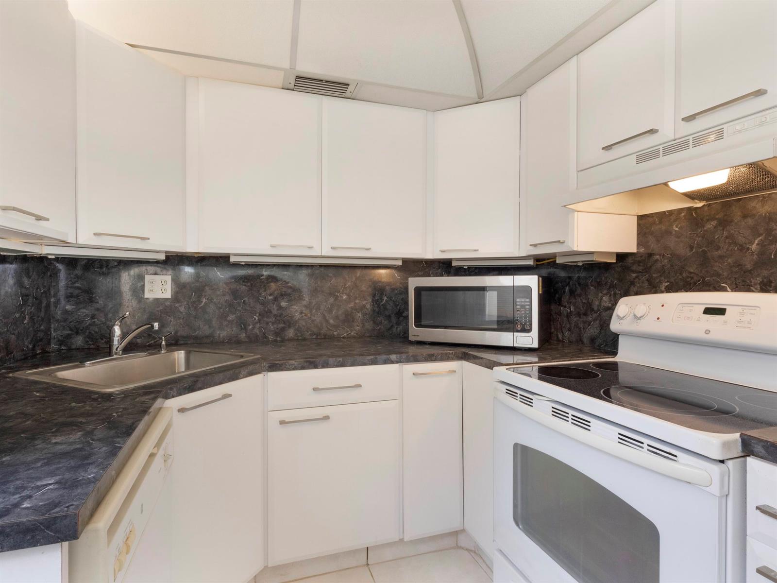 A kitchen features white cabinets, dark marble-look countertops, a stainless steel microwave, and white appliances — 405 Burgundy I, Delray Beach FL 33484, DELRAY BEACH, FL