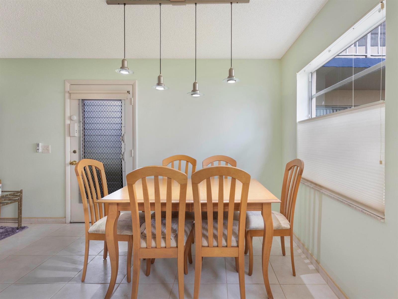 A dining room features a wooden table with six chairs under four pendant lights — 405 Burgundy I, Delray Beach FL 33484, DELRAY BEACH, FL