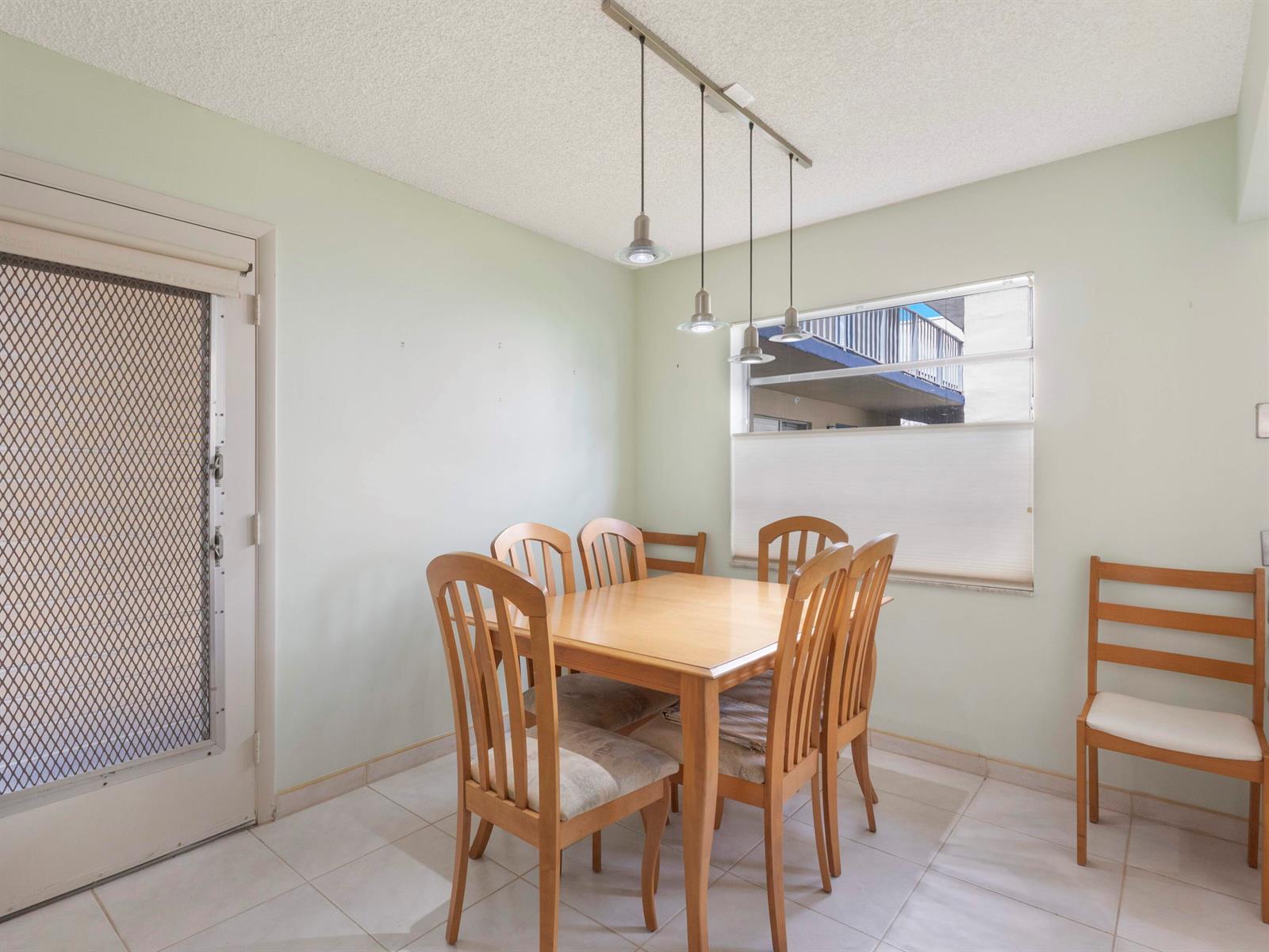 A dining room features a wooden table, six chairs, pendant lighting, and a tiled floor — 405 Burgundy I, Delray Beach FL 33484, DELRAY BEACH, FL