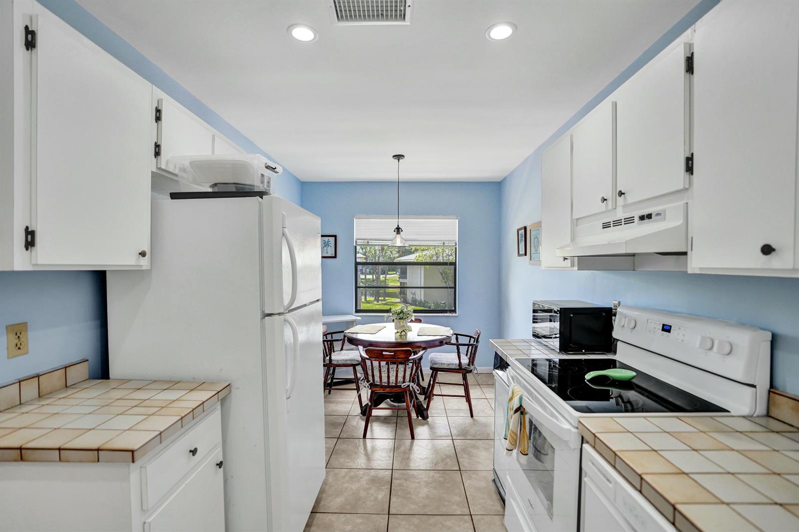 A kitchen with white cabinets, tiled countertops, and a dining area with a window view — 19 Stratford Drive E Unit F, Boynton Beach FL 33436, BOYNTON BEACH, FL