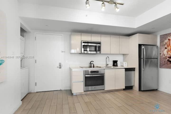 A modern kitchen features light-colored cabinetry, stainless steel appliances, and light wood-look tile flooring — 2602 E Hallandale Beach Blvd # R2006, Hallandale Beach FL 33009, HALLANDALE BEACH, FL