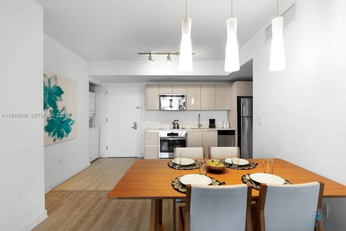 A dining area with a wooden table leads into a kitchen with light-colored cabinets — 2602 E Hallandale Beach Blvd # R2006, Hallandale Beach FL 33009, HALLANDALE BEACH, FL