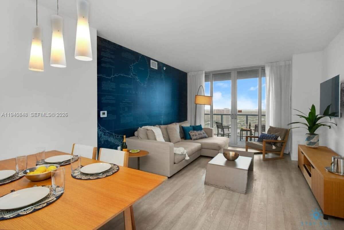 A modern living and dining area features a blue map wall, sectional sofa, and balcony — 2602 E Hallandale Beach Blvd # R2006, Hallandale Beach FL 33009, HALLANDALE BEACH, FL