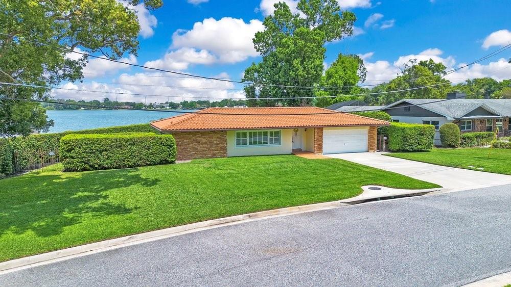 A single-story house with a tile roof and attached garage sits beside a lake — 3108 TROY DRIVE, ORLANDO, FL