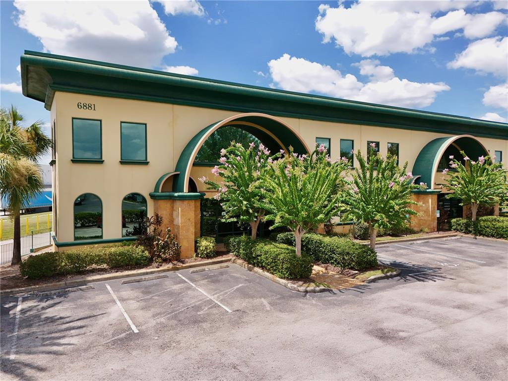 A two-story commercial building features arched entryways, green trim, and a paved parking lot — 6881 KINGSPOINTE PARKWAY UNIT 1&2, ORLANDO, FL