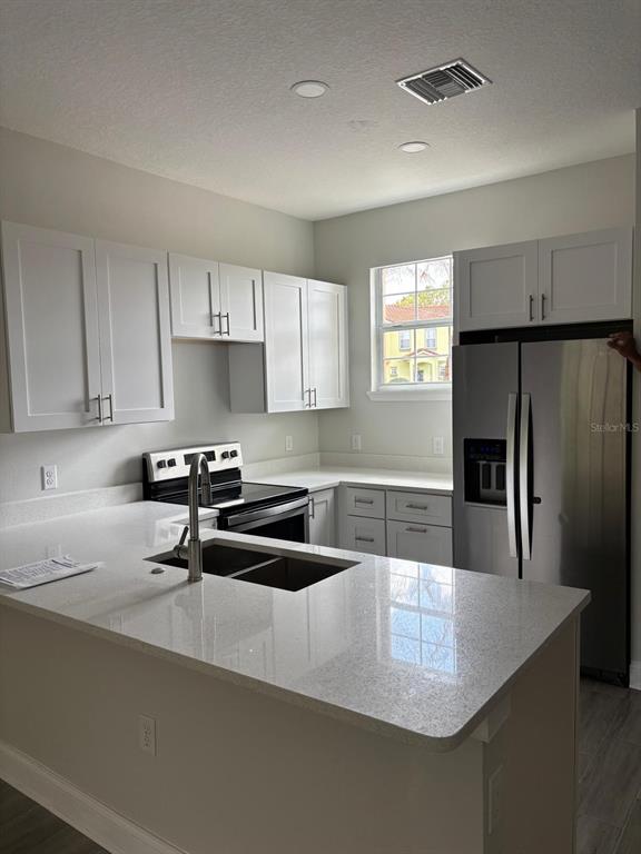 A kitchen features white cabinets, quartz countertops, a stainless steel refrigerator, and a double sink — 427 MADISON CIRCLE, DAVENPORT, FL