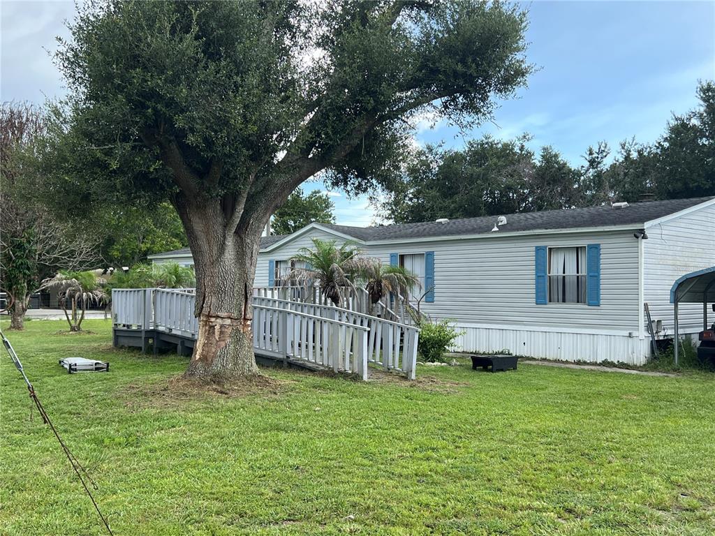 A single-story manufactured home features a large tree in the yard and a wooden ramp — 3760 KAISER AVENUE, ST CLOUD, FL