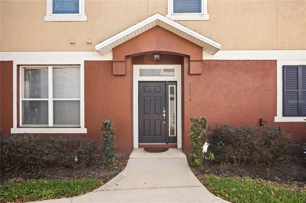A front entrance with a dark door, a concrete walkway, and landscaping against a stucco exterior — 2210 SAN JACINTO CIRCLE, SANFORD, FL