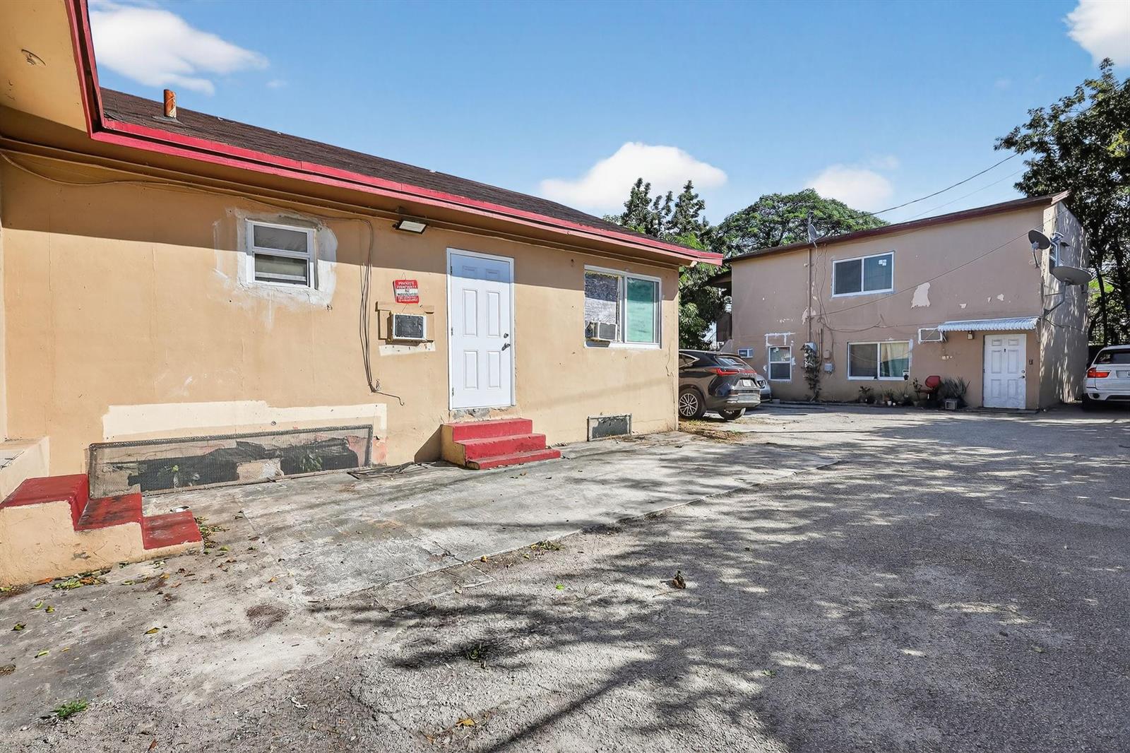 An exterior view of two tan apartment buildings with a shared concrete parking area — 2168 NW 28 Street, Miami FL 33142, MIAMI, FL