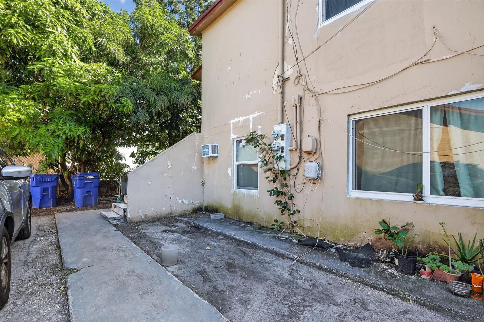 Exterior view of a beige building with a concrete walkway, utility meters, and potted plants — 2168 NW 28 Street, Miami FL 33142, MIAMI, FL