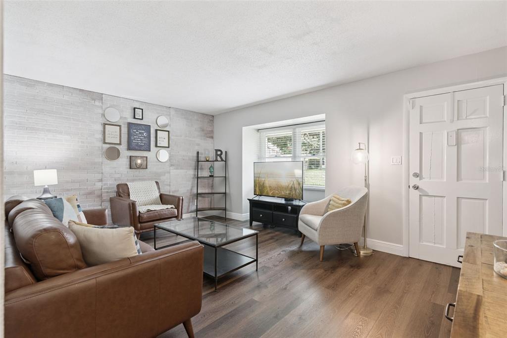 A living room features wood-look flooring, a white brick accent wall, and a leather sofa — 820 PARK LAKE CIRCLE UNIT 11, MAITLAND, FL