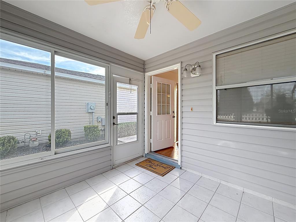A sunroom with gray siding, white tile flooring, a ceiling fan, and a glass door — 1626 GIBBES WAY, THE VILLAGES, FL