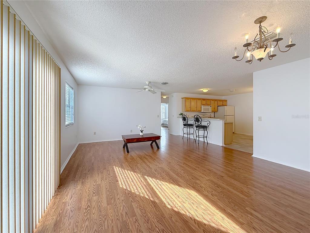 A living room with wood-look flooring, a ceiling fan, and an open kitchen with bar seating — 1626 GIBBES WAY, THE VILLAGES, FL