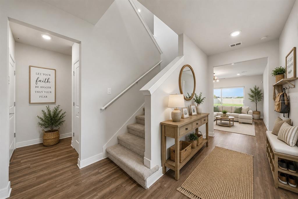 A bright entryway features a staircase, a wooden console table, and a view into the living room — 9018 RALLY SPRING LOOP, WESLEY CHAPEL, FL