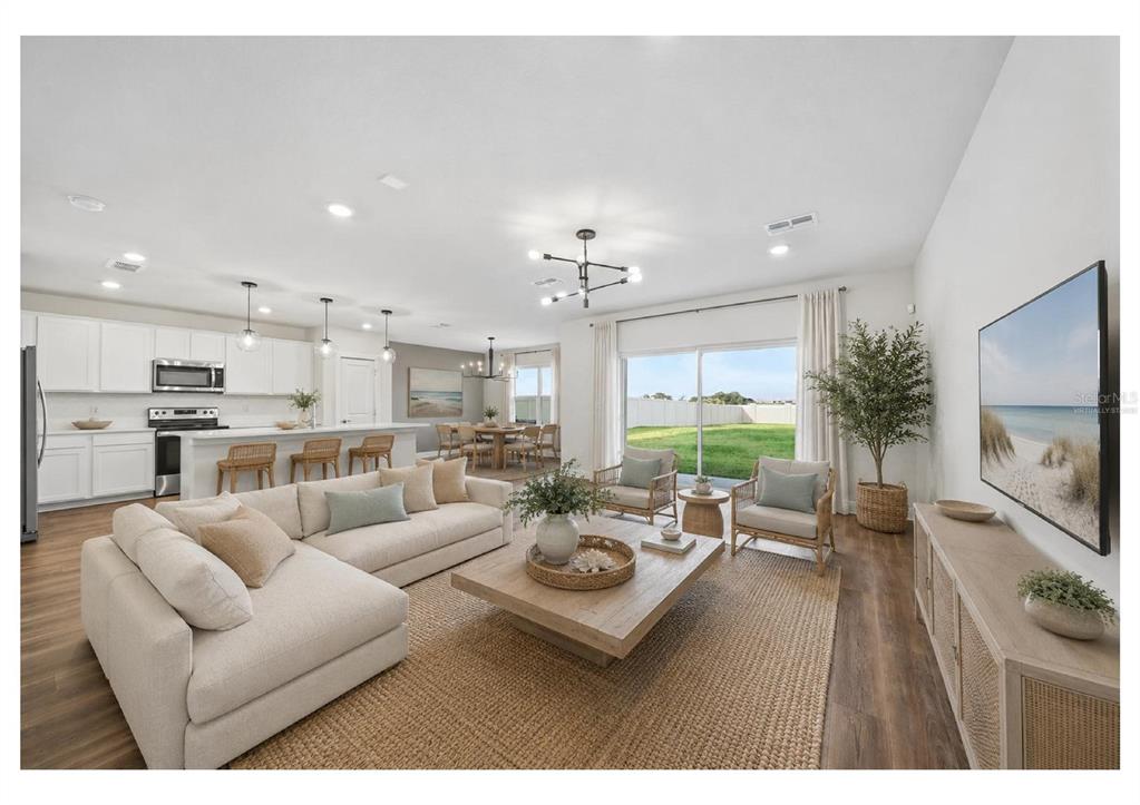 A bright open-concept living room and kitchen featuring light wood floors and neutral furniture — 9018 RALLY SPRING LOOP, WESLEY CHAPEL, FL