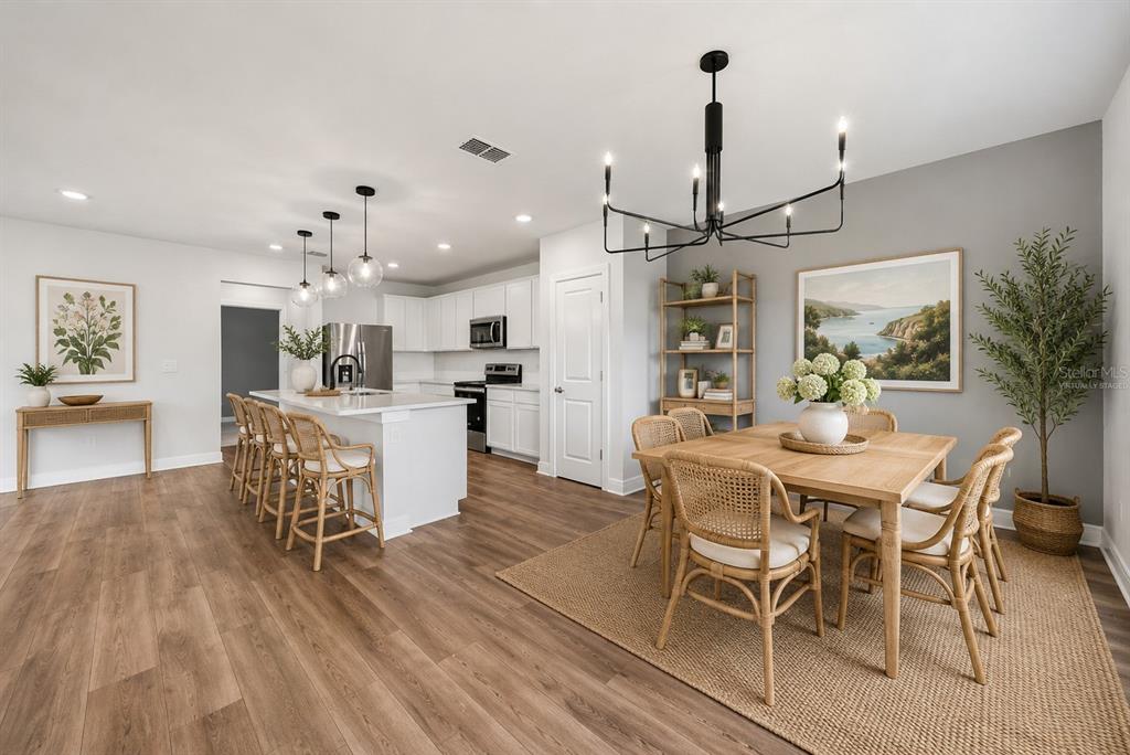 A kitchen and dining area features white cabinetry, a center island, and wood-look flooring — 9018 RALLY SPRING LOOP, WESLEY CHAPEL, FL