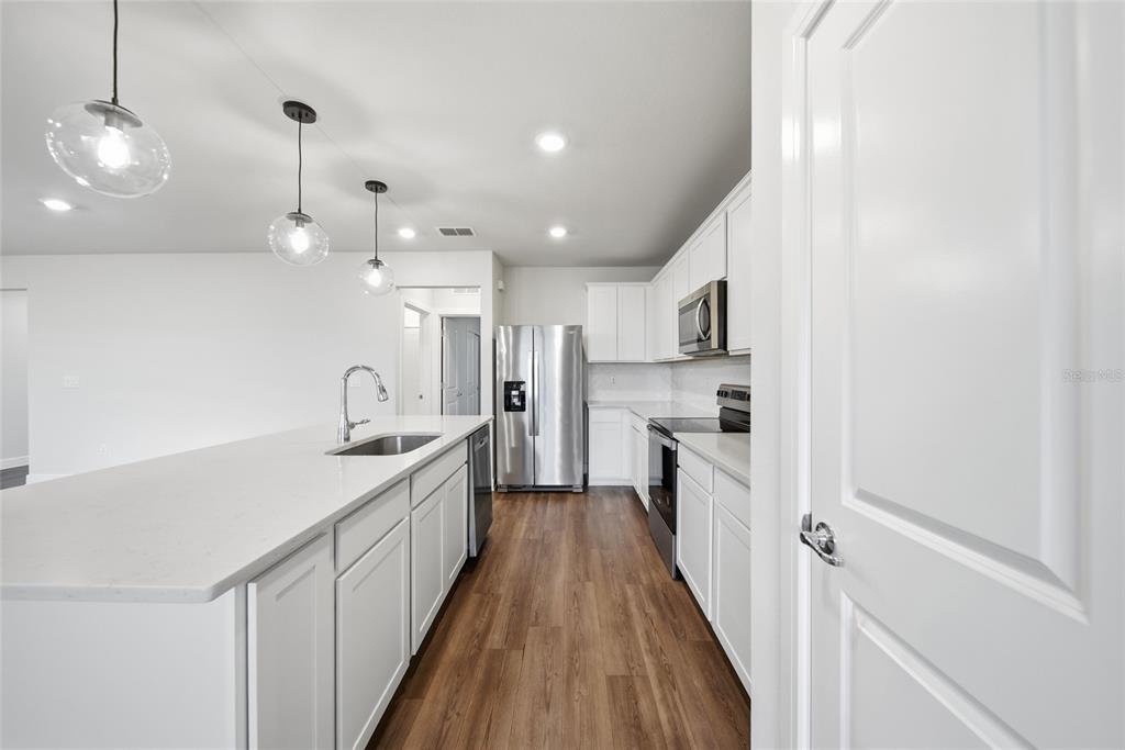 A modern kitchen features white cabinets, stainless steel appliances, and a large island with seating — 9018 RALLY SPRING LOOP, WESLEY CHAPEL, FL