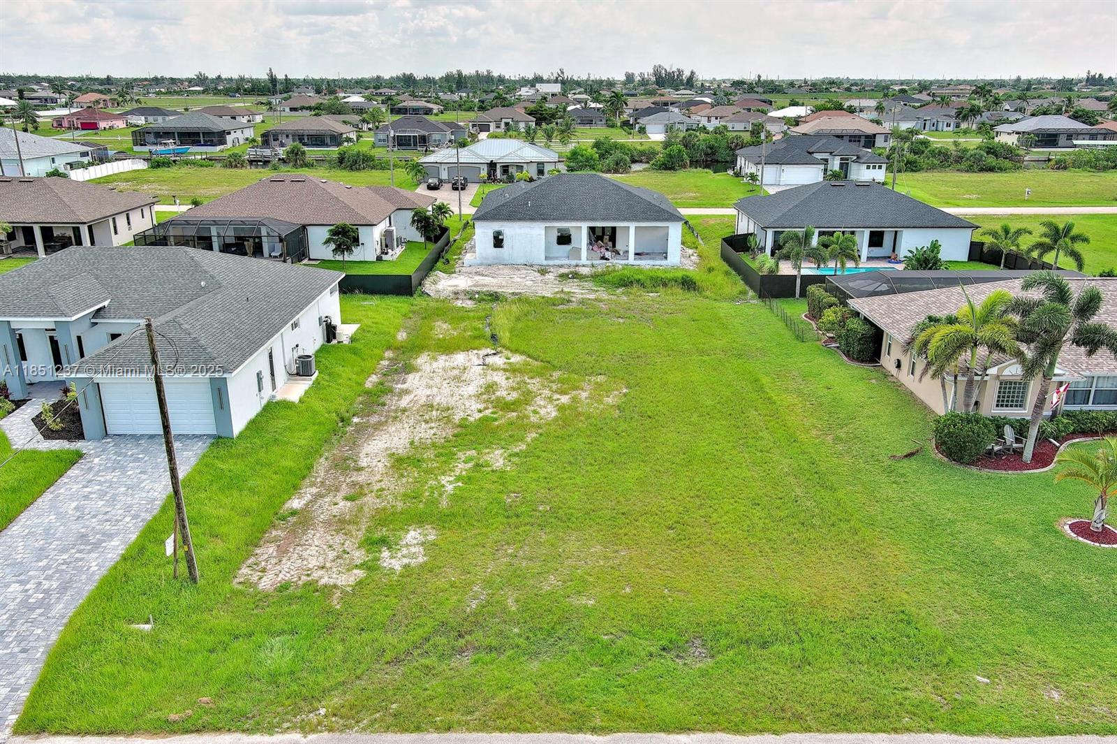An aerial view shows a vacant residential lot situated between two existing houses — 1025 NW 35th Place, Cape Coral FL 33993, CAPE CORAL, FL