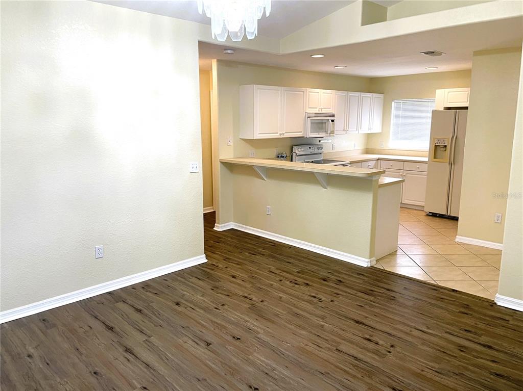 A kitchen with white cabinets and a breakfast bar overlooks a room with wood flooring — 2498 MARGARET LANE, NORTH PORT, FL
